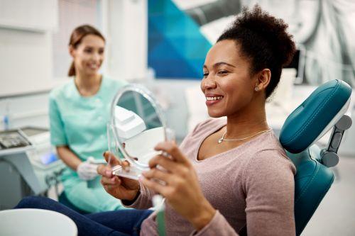 woman sitting in a dental chair while holding a mirror
