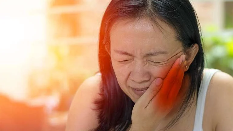 Woman wincing and holding her jaw from tooth pain