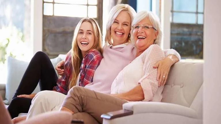 Three generations of women smiling together on a sofa
